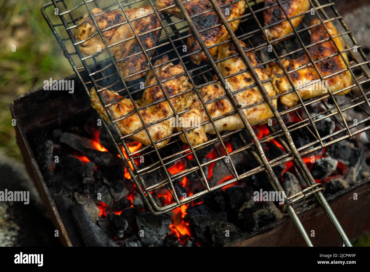 Chicken wings in metal grate grilling on a brazier with flaming
