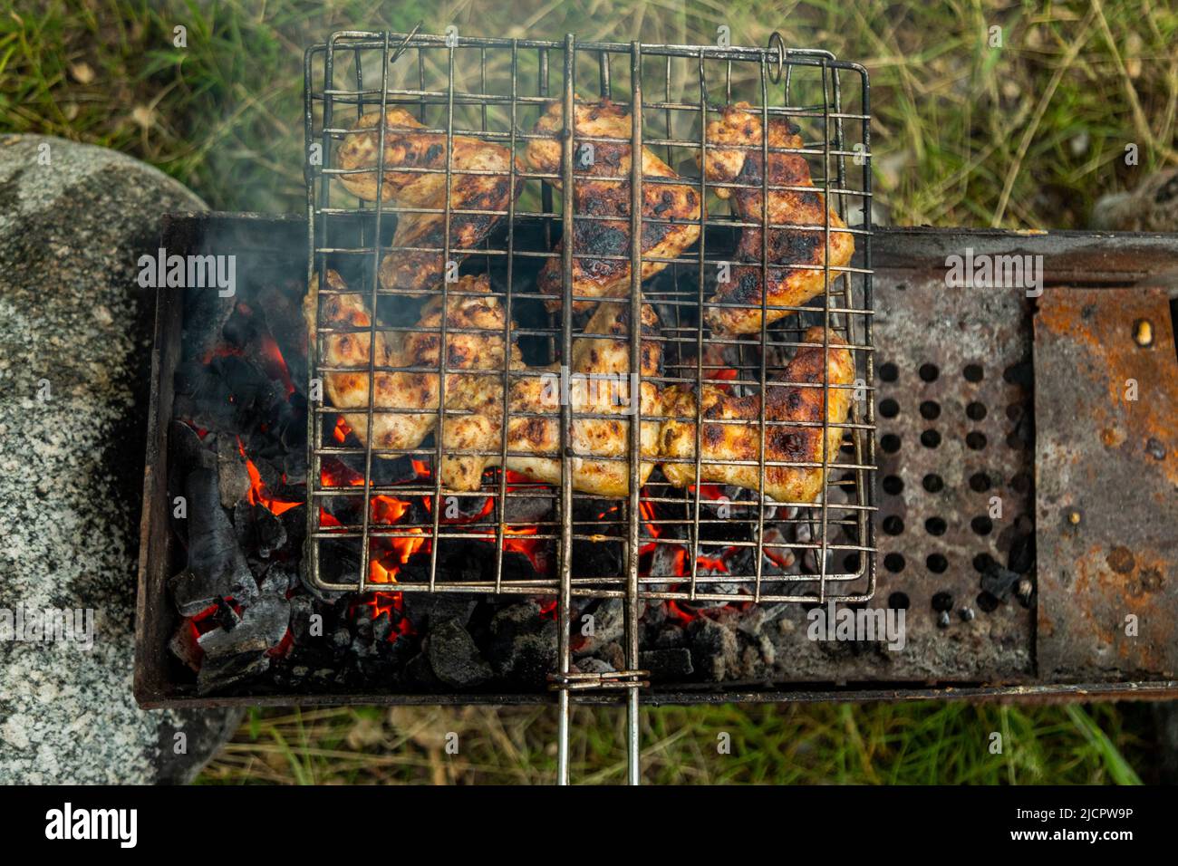 Top down view chicken wings in metal grate grilling on a brazier with