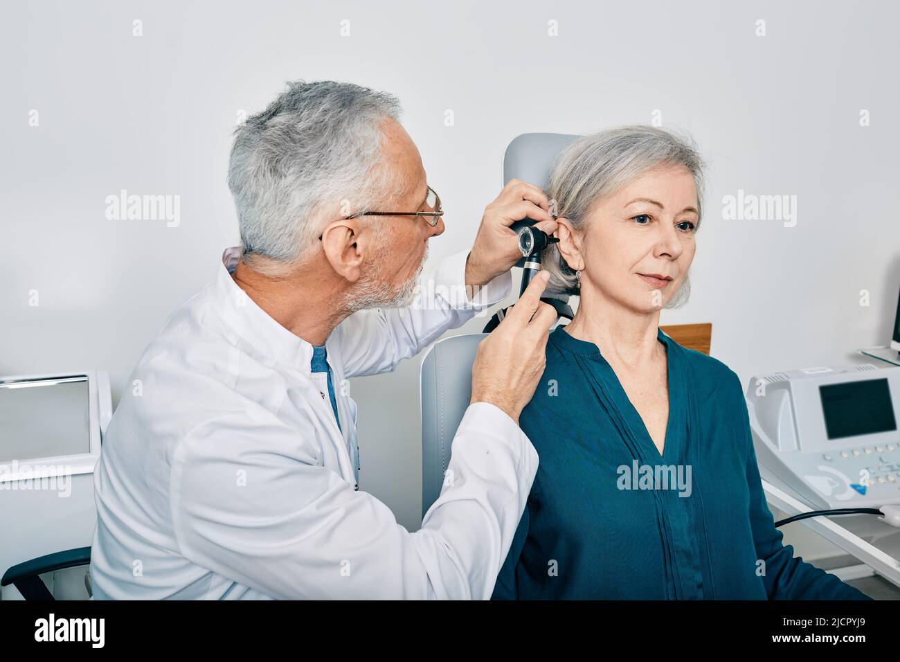 Otolaryngologist doctor checking senior woman's ear using otoscope or auriscope at hearing center. Audiology Stock Photo