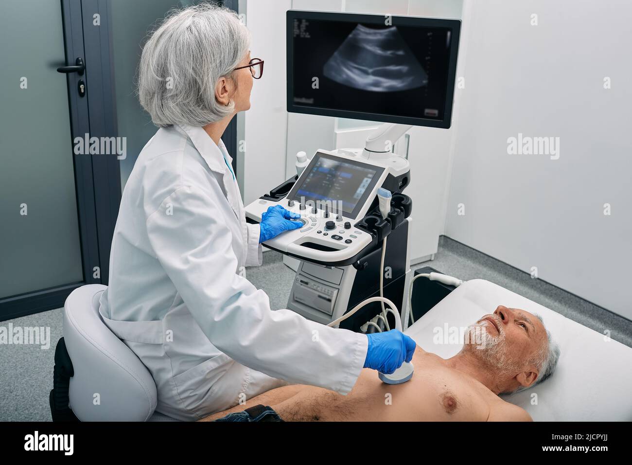 Heart ultrasound exam for senior man with ultrasound specialist while medical exam at hospital Stock Photo