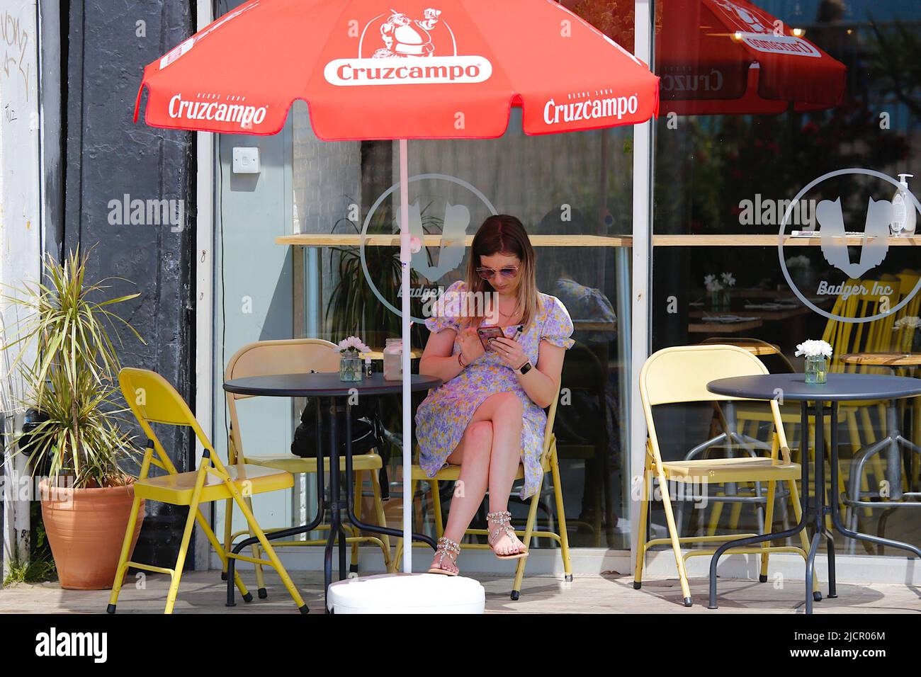 Hastings, East Sussex, UK. 15 Jun, 2022. UK Weather: Hot and sunny at the seaside town of Hastings in East Sussex as Brits enjoy the warm weather today along the seafront promenade. A young woman sits in the shade enjoying a drink. Photo Credit: Paul Lawrenson /Alamy Live News Stock Photo