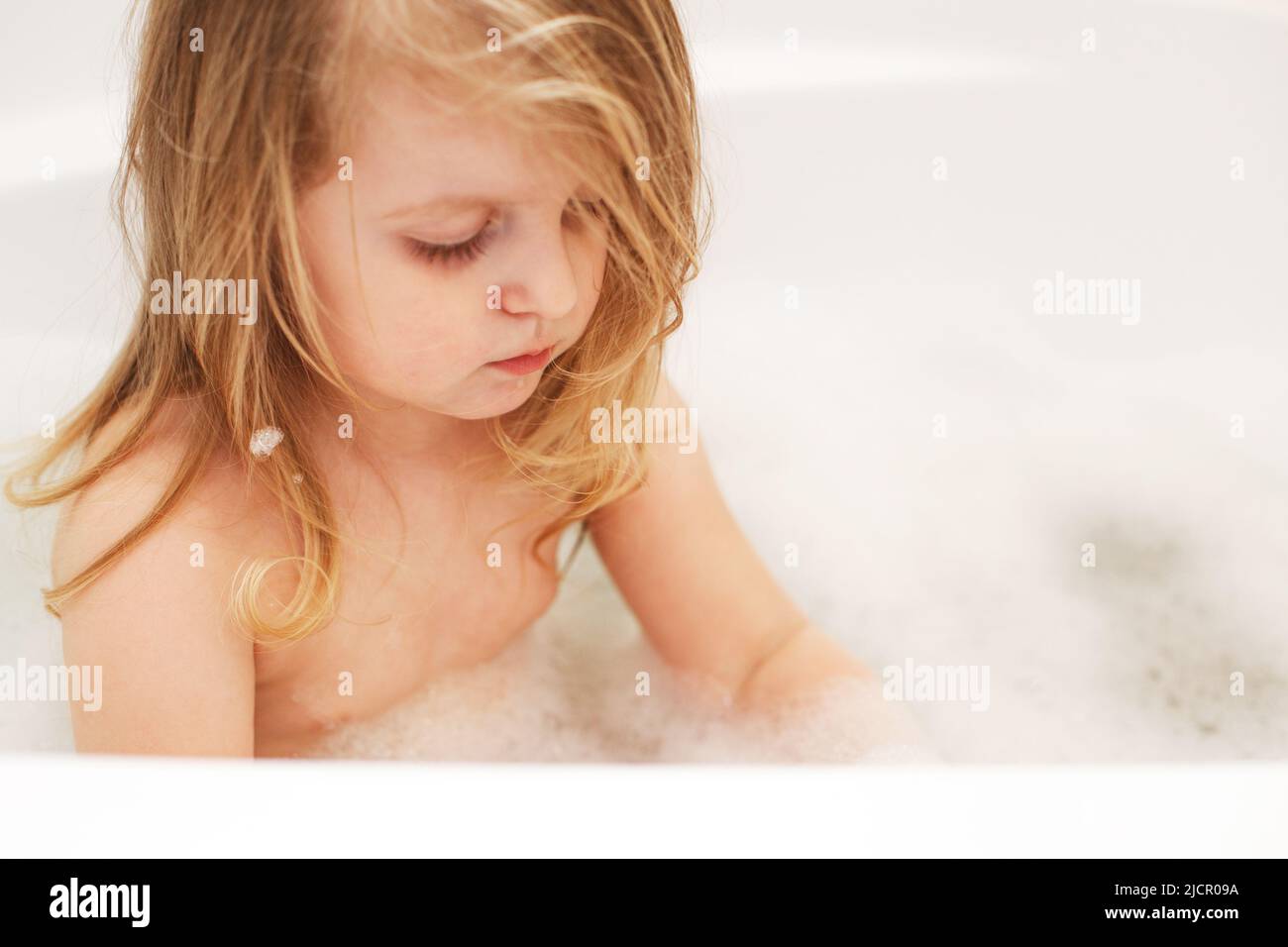 Funny little baby girl with blond hair playing with foam in a bath tub Stock Photo