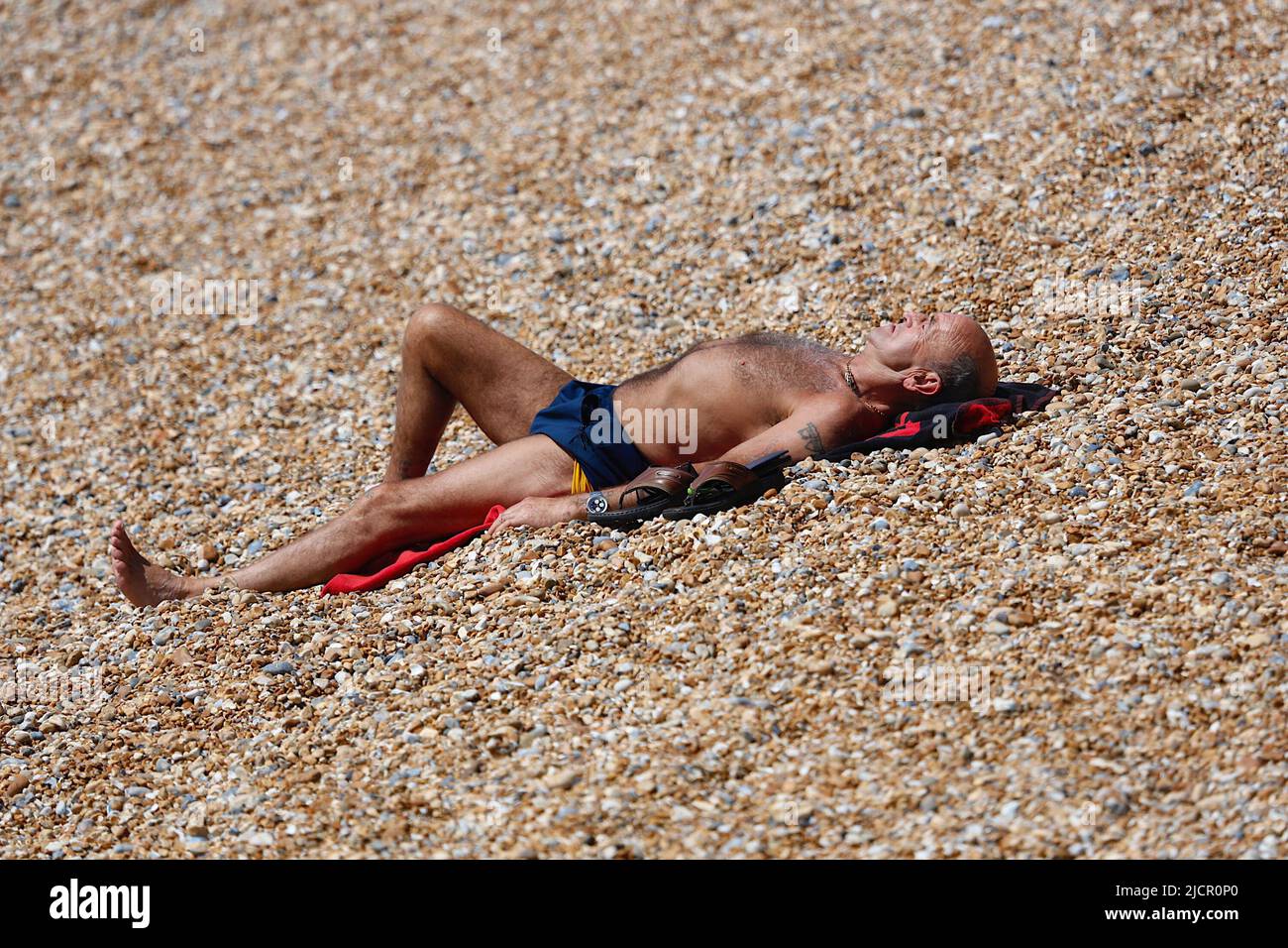 Hastings, East Sussex, UK. 15 Jun, 2022. UK Weather: Hot and sunny at the seaside town of Hastings in East Sussex as Brits enjoy the warm weather today along the seafront promenade. A man soaks up the rays on the pebble beach. Photo Credit: Paul Lawrenson /Alamy Live News Stock Photo