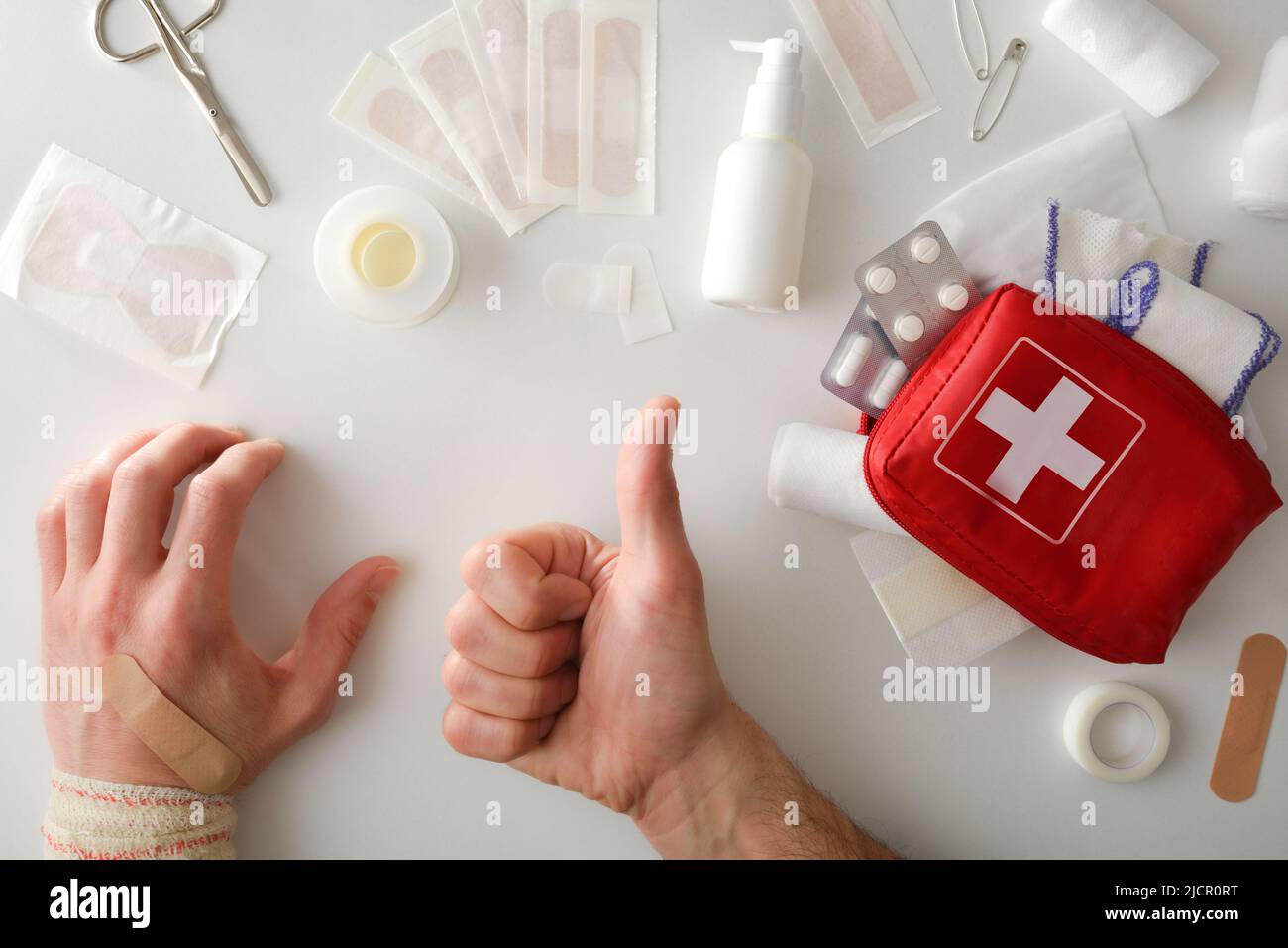 Heal successfully with portable first aid equipment on the table and hand with ok gesture and bandaged hand. Horizontal composition. Top view. Stock Photo