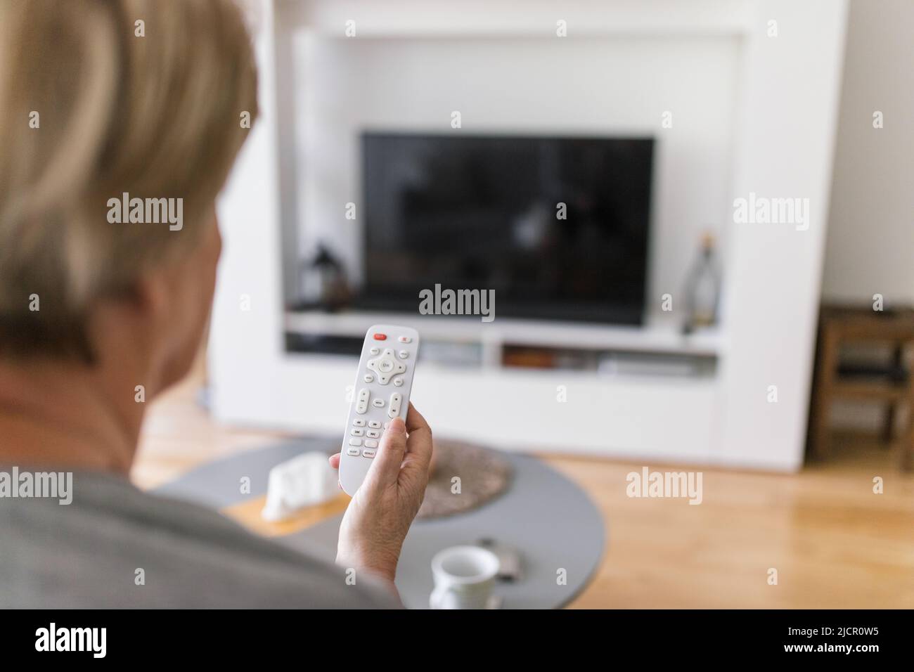 Senior woman with remote control watching television Stock Photo