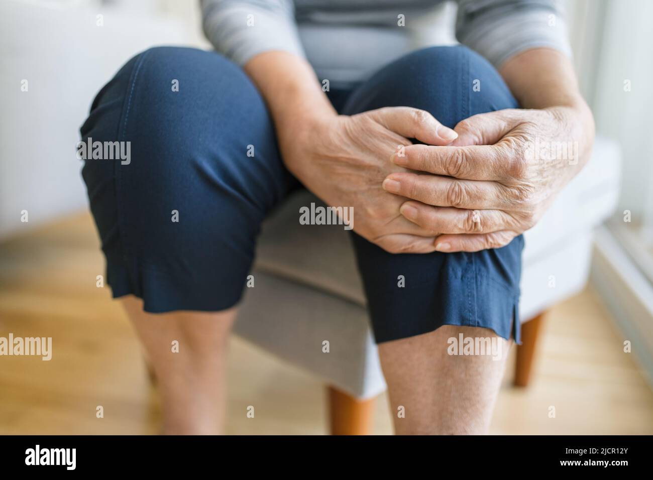 Senior woman sitting on bench, holding her painful knee Stock Photo