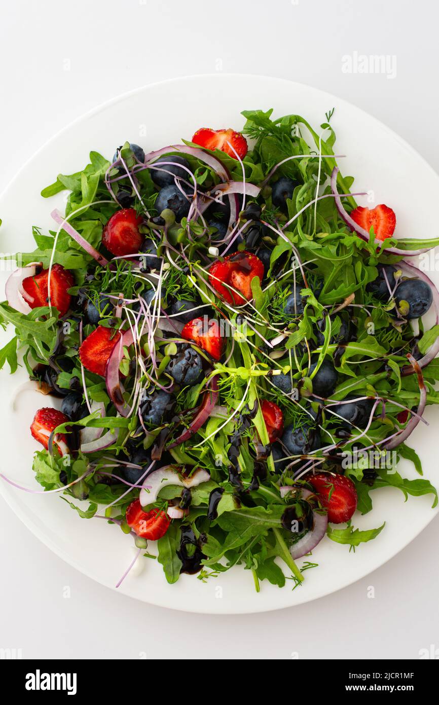 Light salad with arugula and berries, strawberries and blueberries, delicious healthy summer salad on a white background Stock Photo