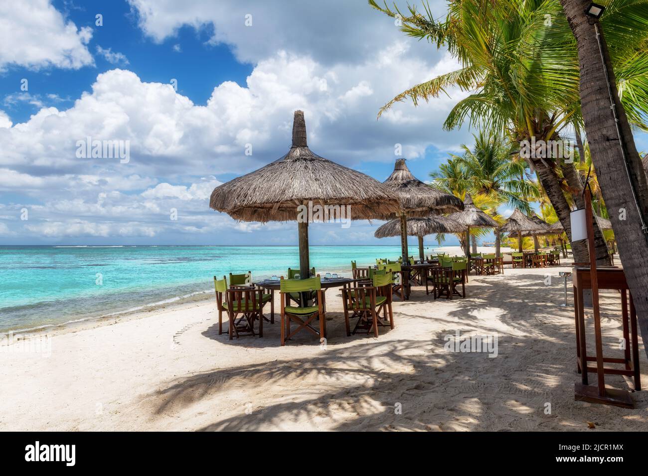 Beach cafe on sandy beach under straw umbrella, palm trees and beautiful sea on exotic tropical island. Stock Photo