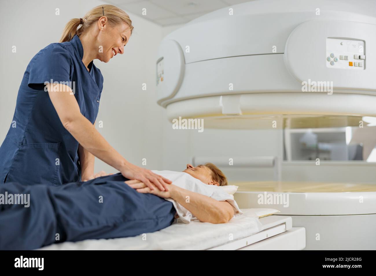 Radiologist controls MRI or CT or PET Scan with female patient undergoing procedure Stock Photo