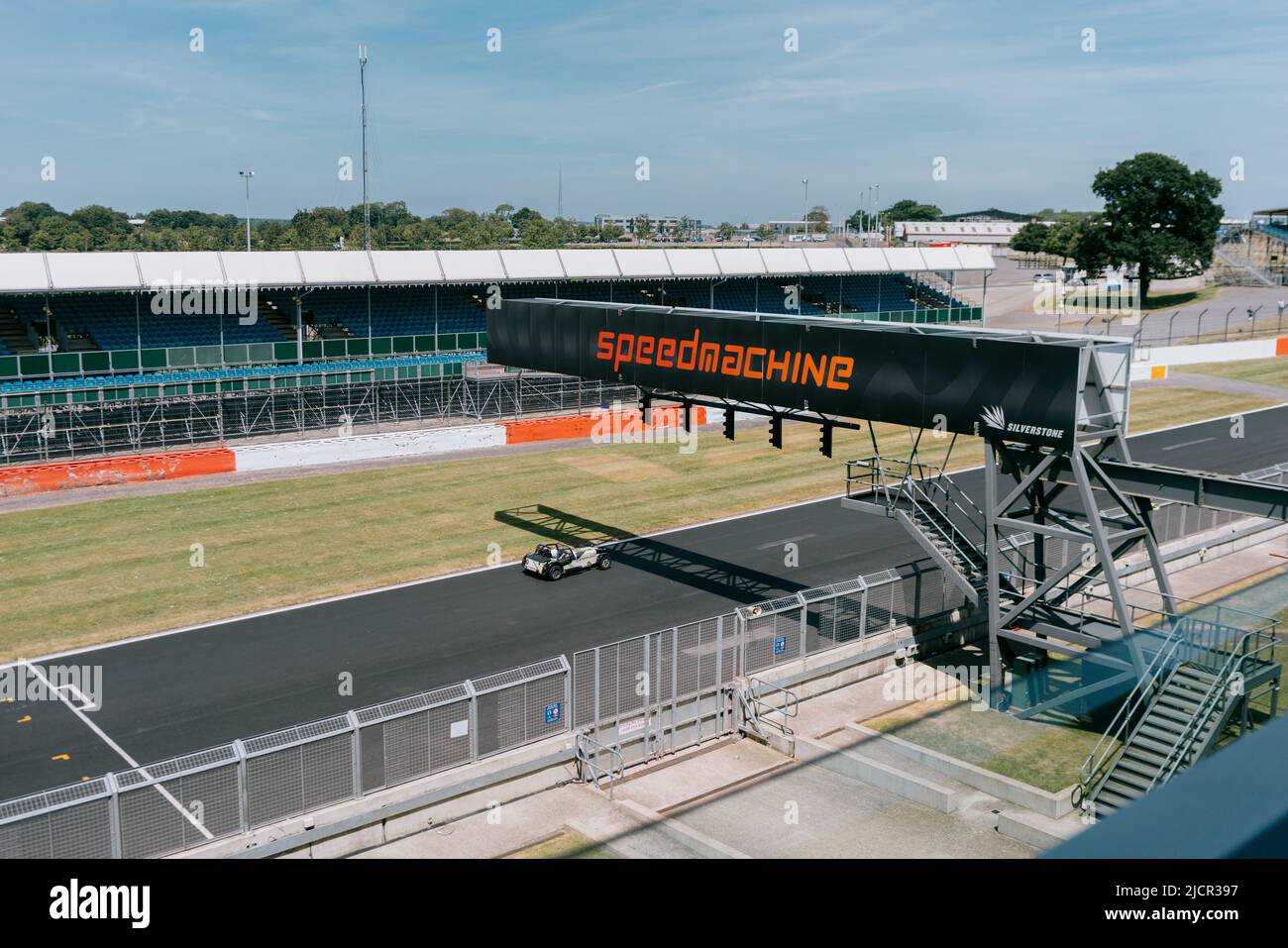 Vintage car races along Hamilton Straight. Under speedmachine gantry sign, on a sunny day at Silverstone Circuit, Northamptonshire, UK. Stock Photo