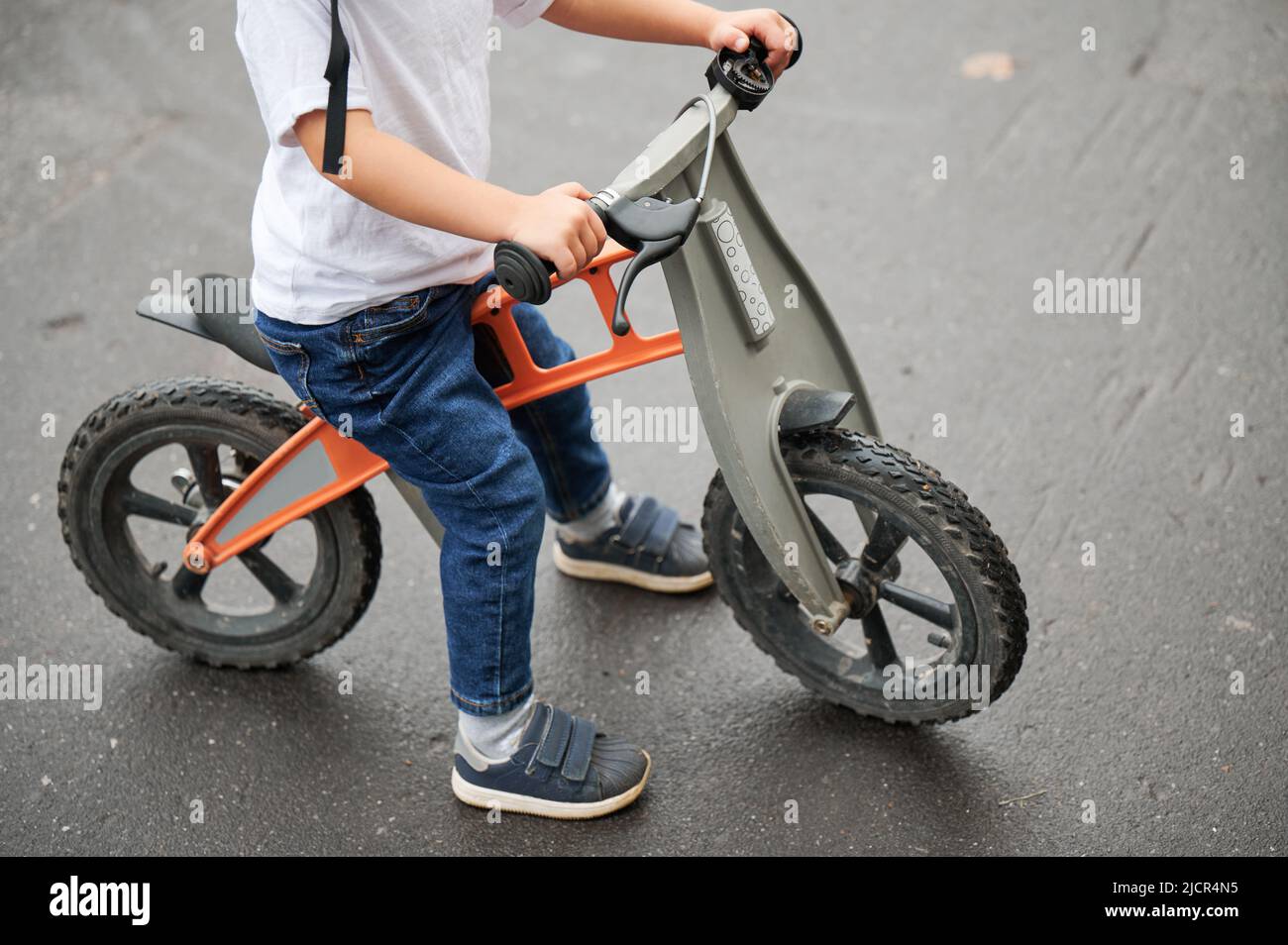 Cropped view of child holding bicycle handlebar while riding balance bike outdoors. Stock Photo