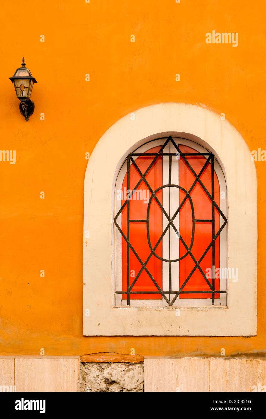 Shuttered, arched window with iron grate set in orange plaster wall in Rome, Italy. Stock Photo