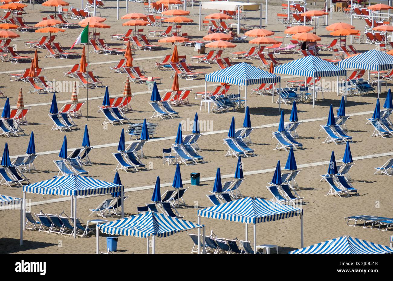 Blue and orange beach umbrellas  and chairs waiting for sunbathers. Stock Photo