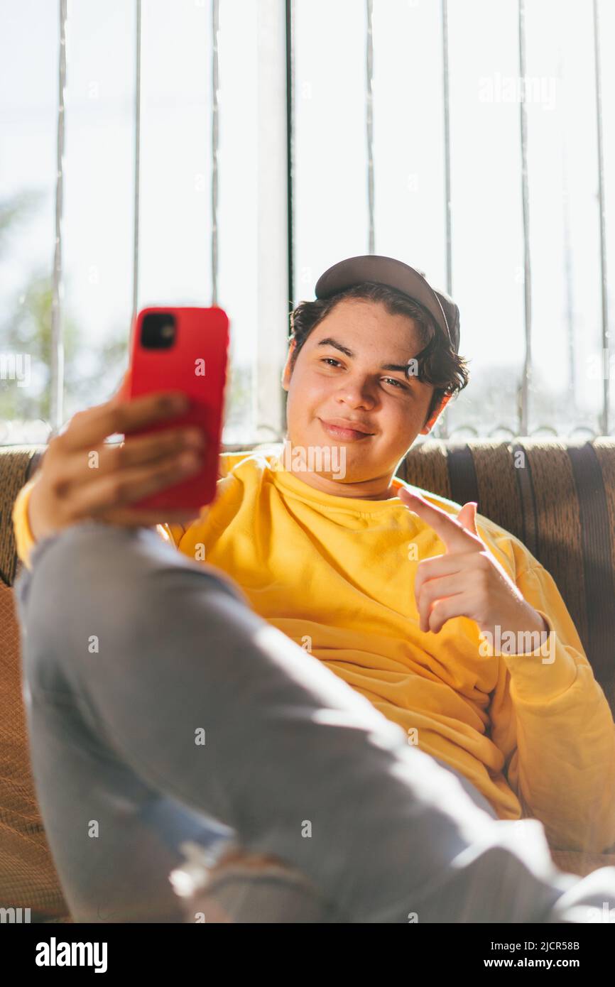 Young person holding his red cell phone and greeting friends by video call. Man talking to family members and greeting them happily Stock Photo