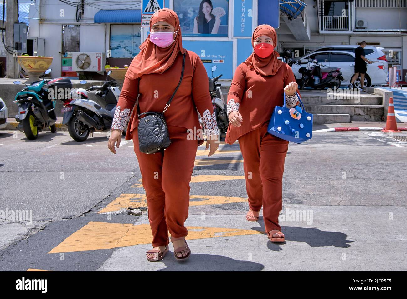 Muslim women in traditional dress and wearing matching orange clothes of Shalwar Kameez with hijab and shawl and face mask Stock Photo
