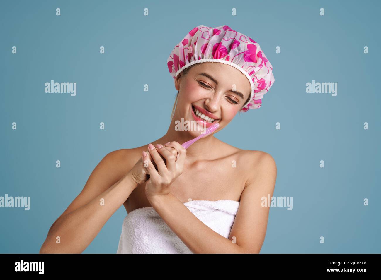 Young woman wearing shower cap smiling while brushing her teeth
