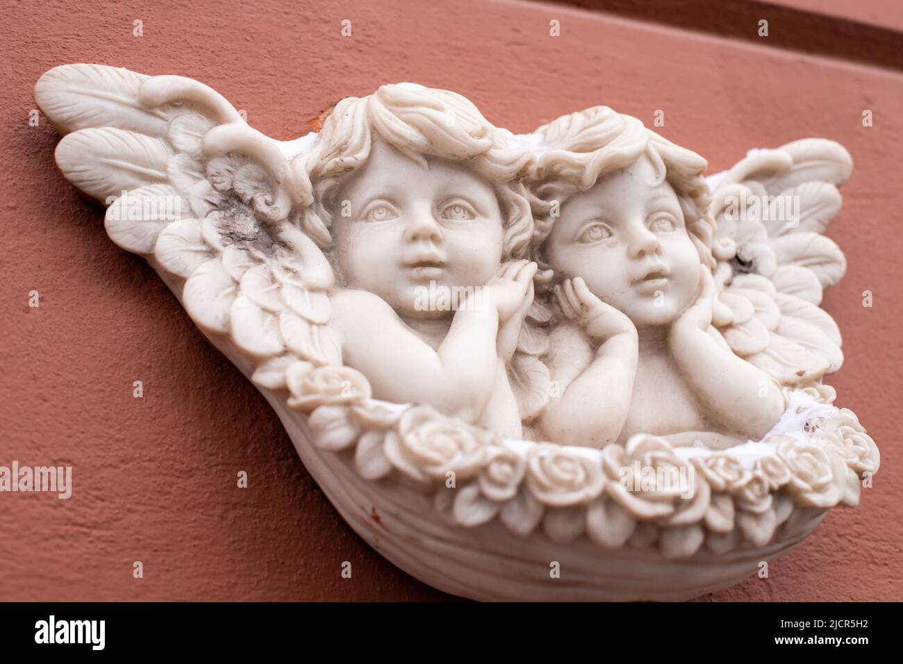 Two baby angels with wings marble sculpture on red wall of building. Close-up, front view. Stock Photo