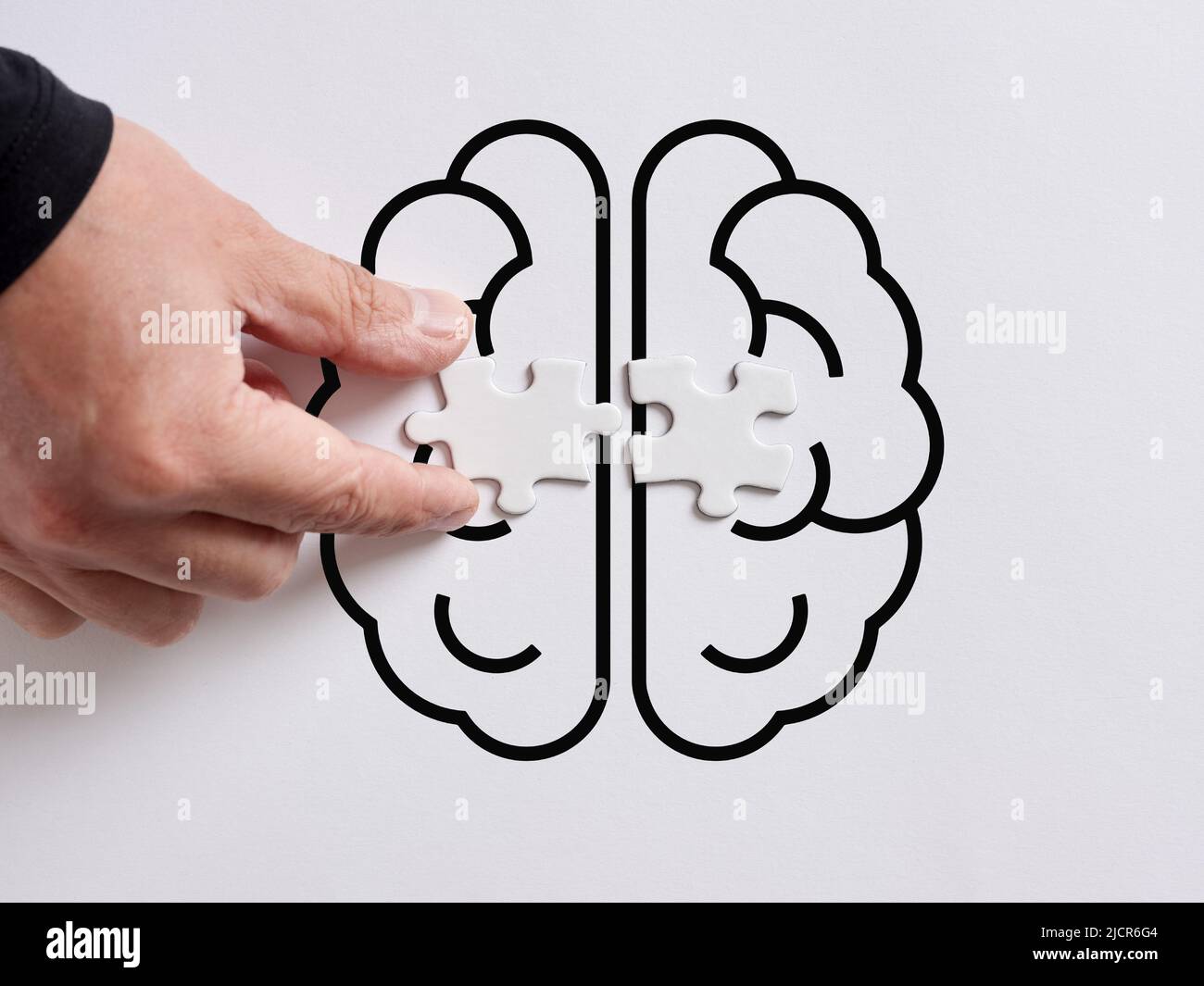 Hand connects the puzzles on the right and left side of human brain symbol. Using or connecting right and left side of the brain. Stock Photo