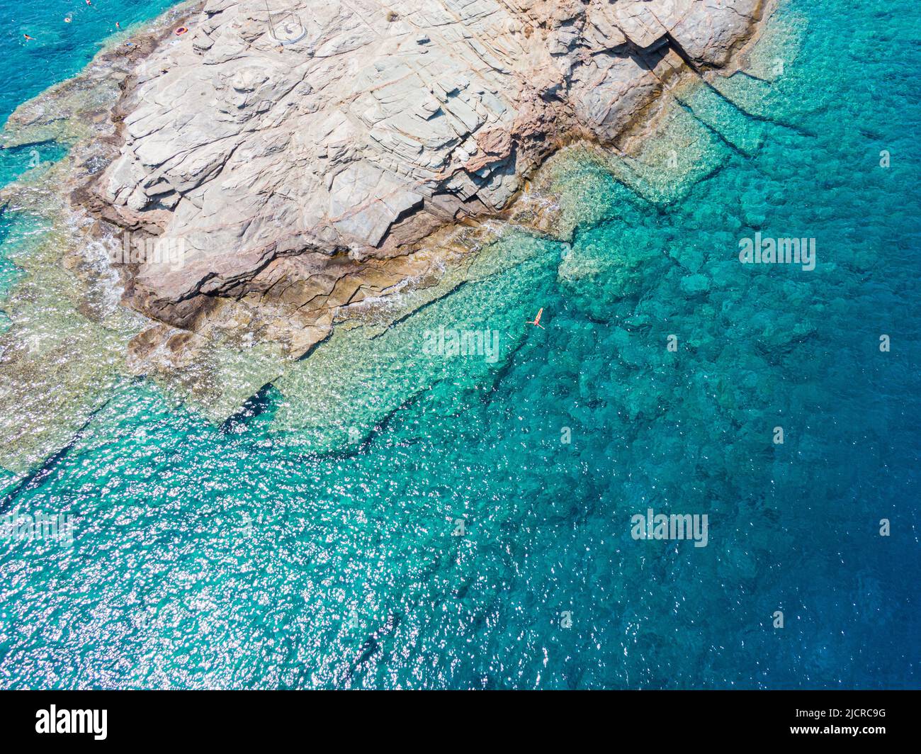 Unrecognizable woman swimming on azure water texture, transparent sea surface with a rocky bottom. Aerial view, natural blue background Stock Photo