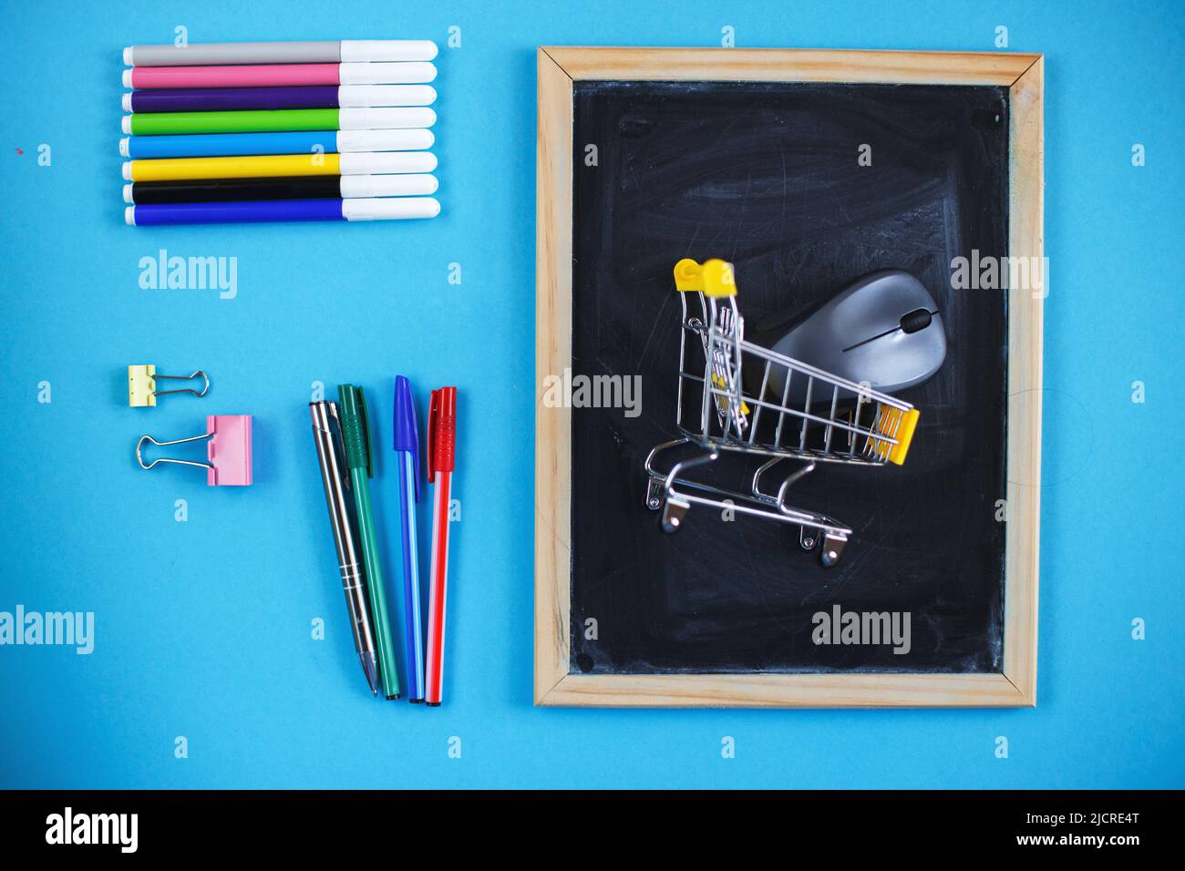 School chalkboard and stationery accessories, pencils and pens with a shopping cart. Back to school concept, top view, blue background Stock Photo