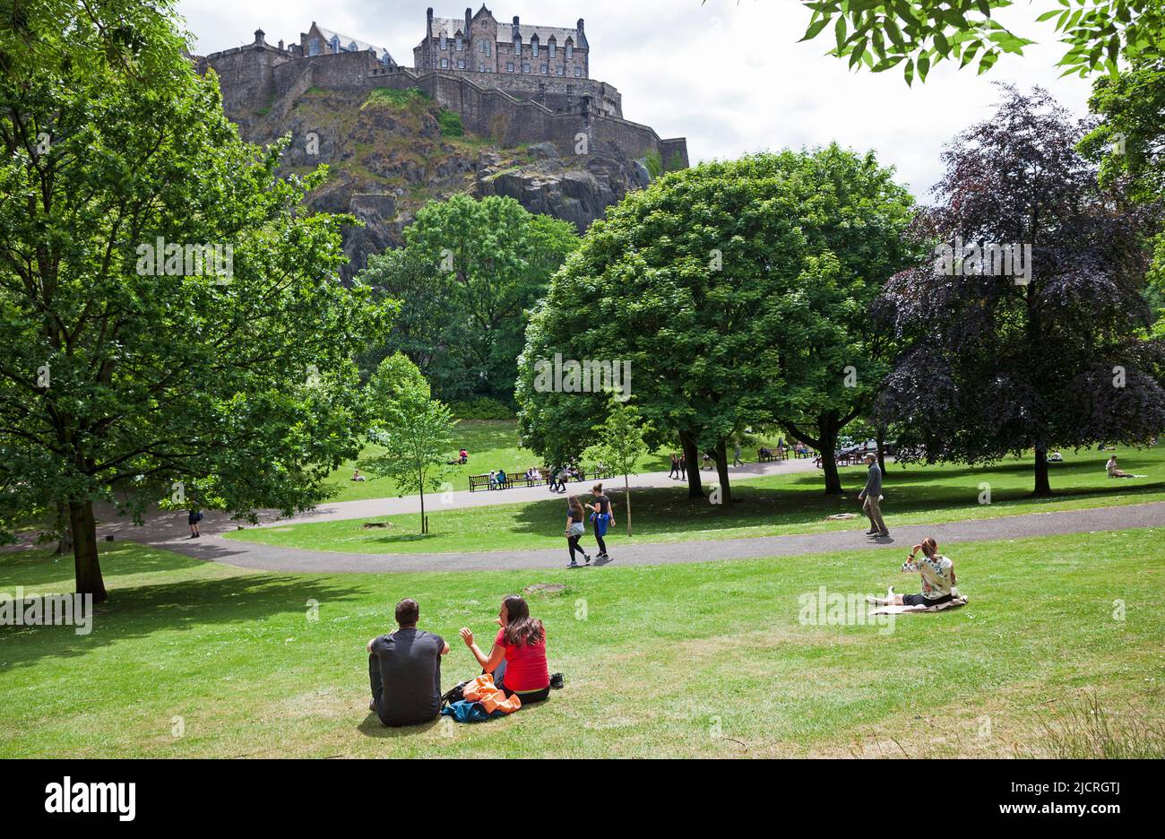 Edinburgh city centre, Scotland, UK. 15.06.2022. Summer arrives in the city after a recent cool cloudy period of weather. Mid-afternoon temperature of 18 degrees centigrade encouraging people out into the city's green spaces. Pictured: People relax in the sunshine in Princes Street Gardens West under the shadow of Edinburgh Castle Credit: Scottishcreative/alamy live news. Stock Photo