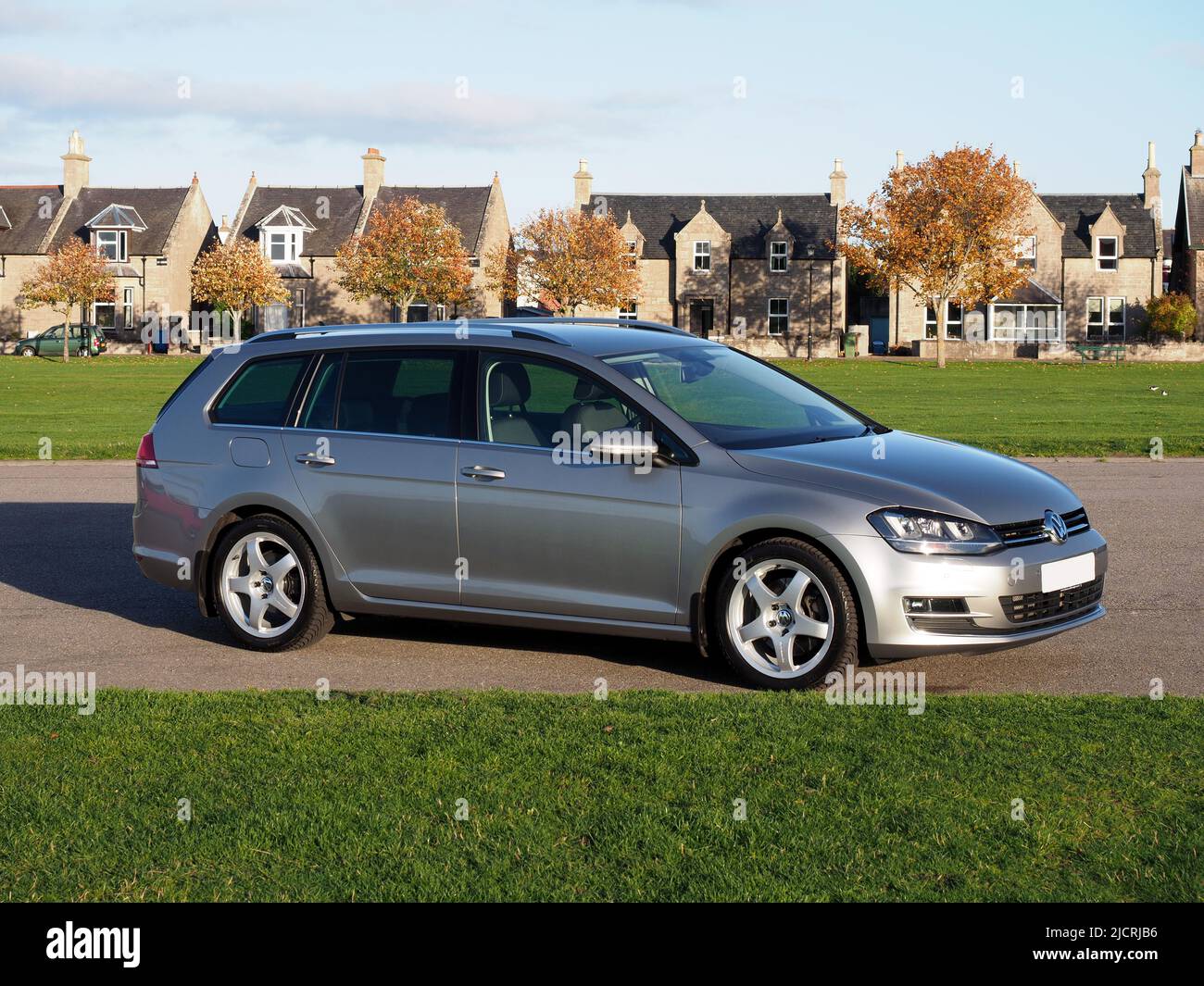 Side view of a Tungsten silver Volkswagen Golf MK7 estate, variant, with Team Dynamics Pro Race 3 Alloys. Parked next to green grass playing fields. Stock Photo