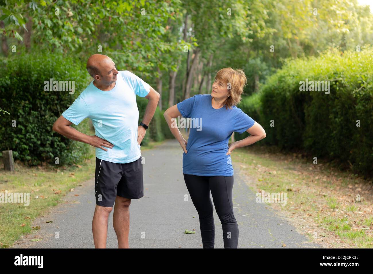 Two mature adults looking to each other while streching their bodies after workout sorrounded by nature in a city park Stock Photo