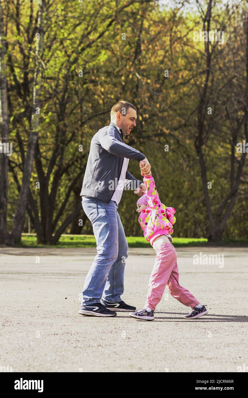 Dad is playing with his daughter in the backyard. Unwinds it around itself. Family, dad plays with his daughter on weekends. Stock Photo