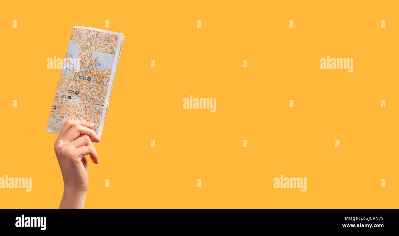 Banner with woman hand holding tourist map, guide on orange background. Travelling, visiting places of interests, attractions concept. Copy space. High quality photo Stock Photo