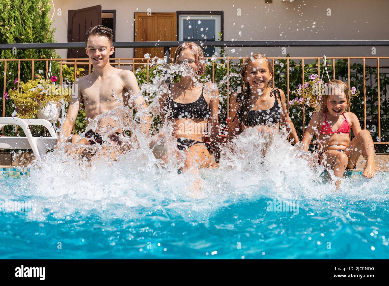 Four happy children having fun in a hotel pool splashing water enjoying summer holidays Stock Photo