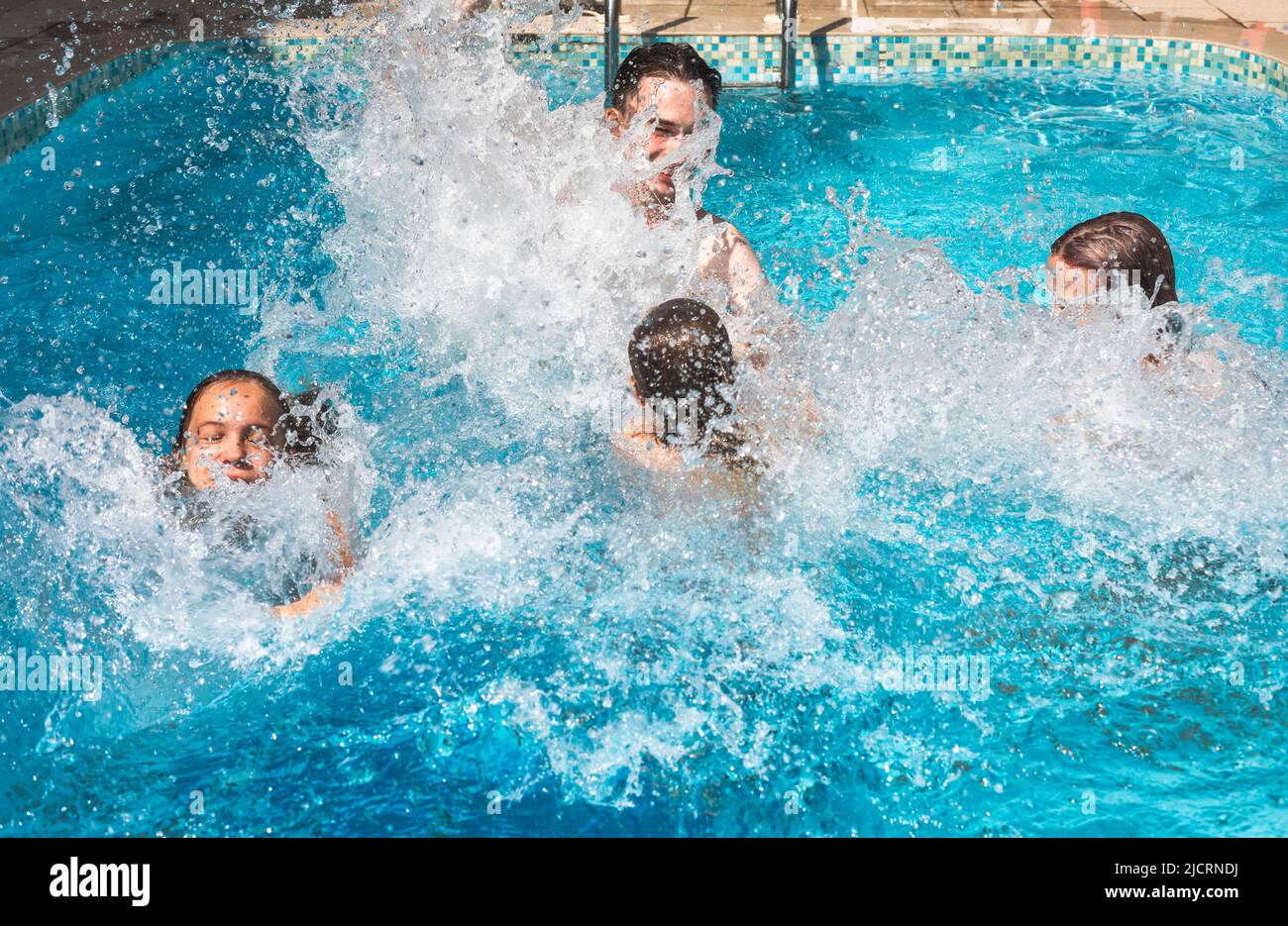 Four happy children having fun in a hotel pool splashing water enjoying summer holidays Stock Photo