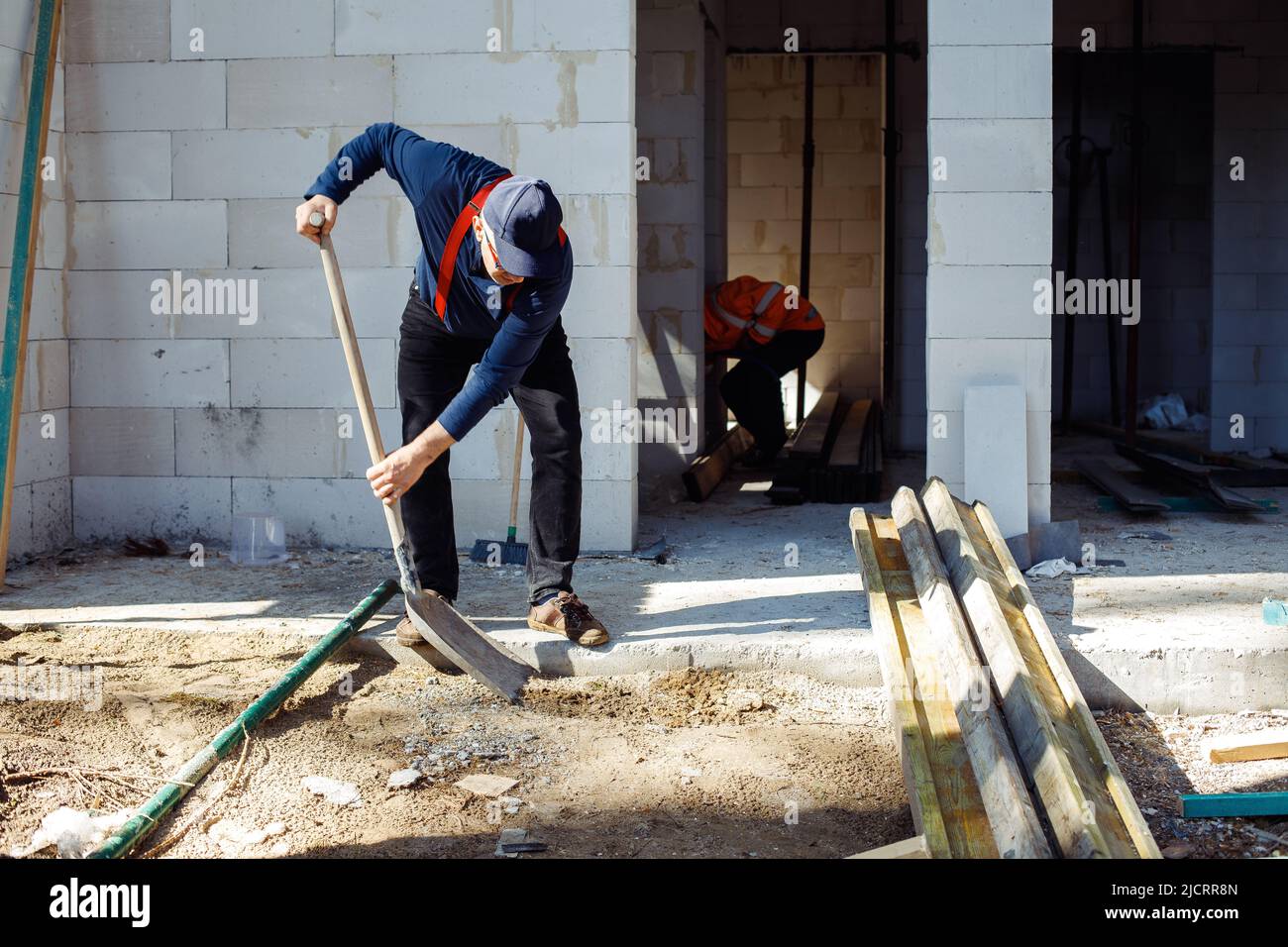 Worker builders, men in uniform and caps, labors, wetbacks preparing basement floor for building, shoveling wood pile Stock Photo