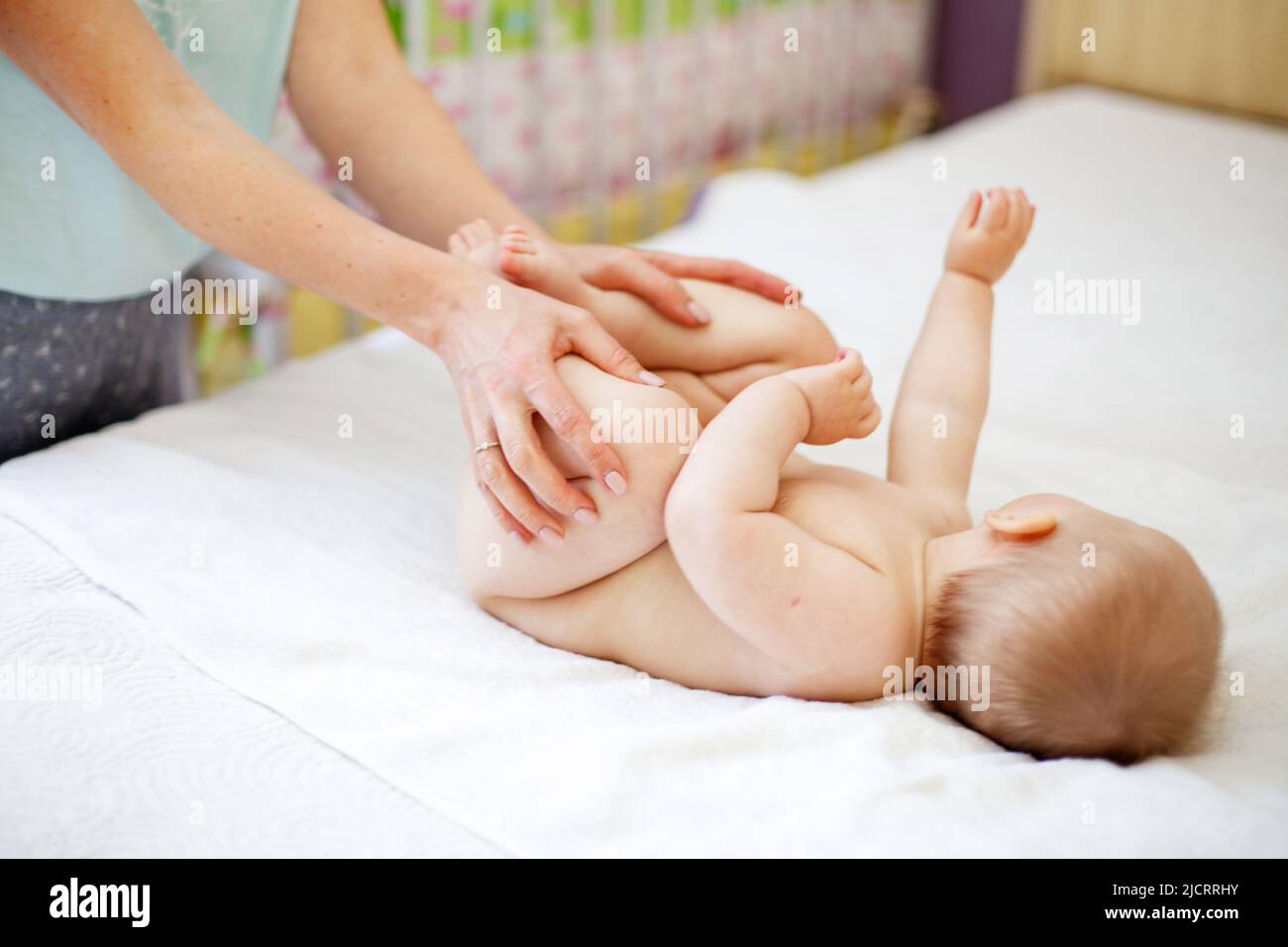 Mom Mom does gymnastics for a child. Mother massaging baby in a bed at home Stock Photo