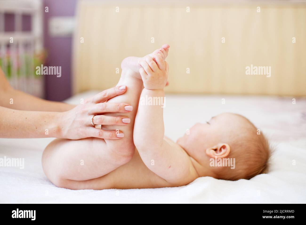 Mom Mom does gymnastics for a child. Mother massaging baby in a bed at home. Mother and baby. Happy family. Mom's love and tenderness. Stock Photo