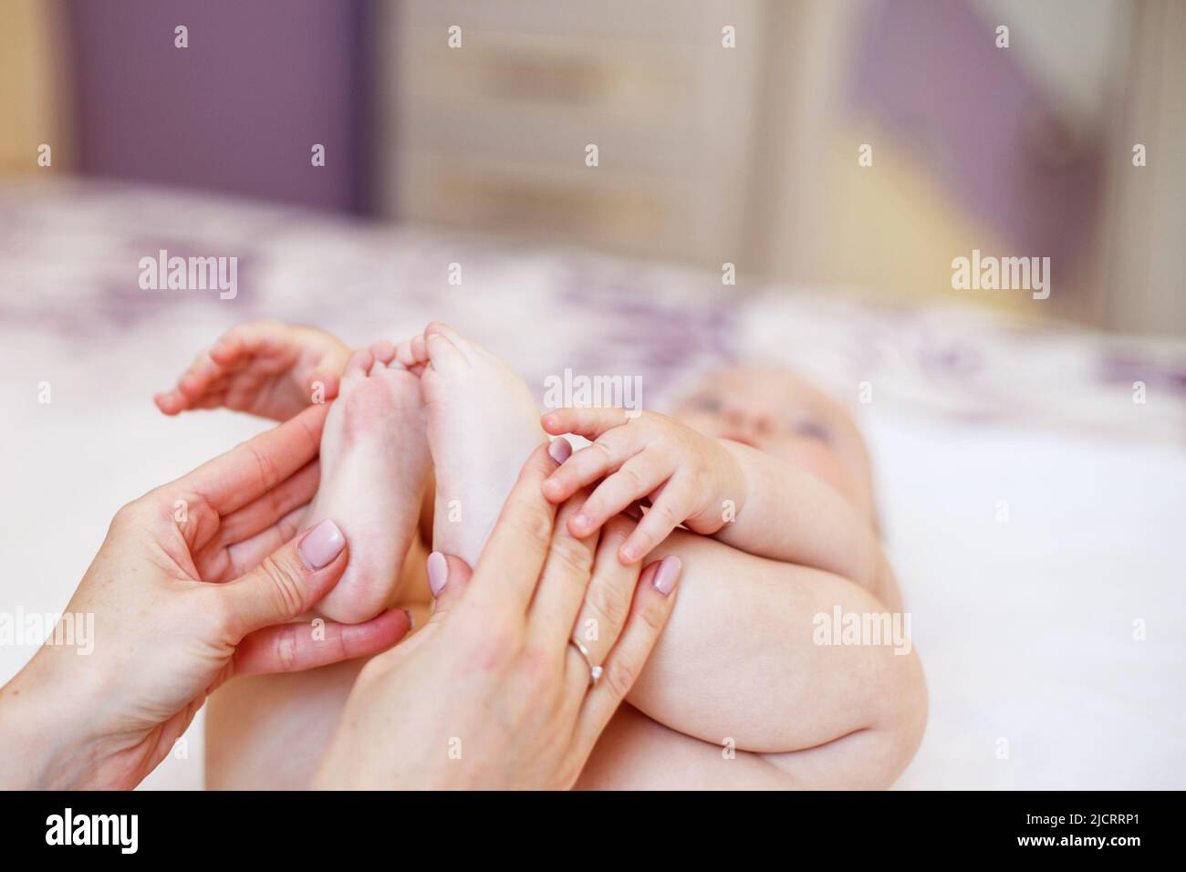 Mom Mom does gymnastics for a child. Mother massaging baby in a bed at home Stock Photo