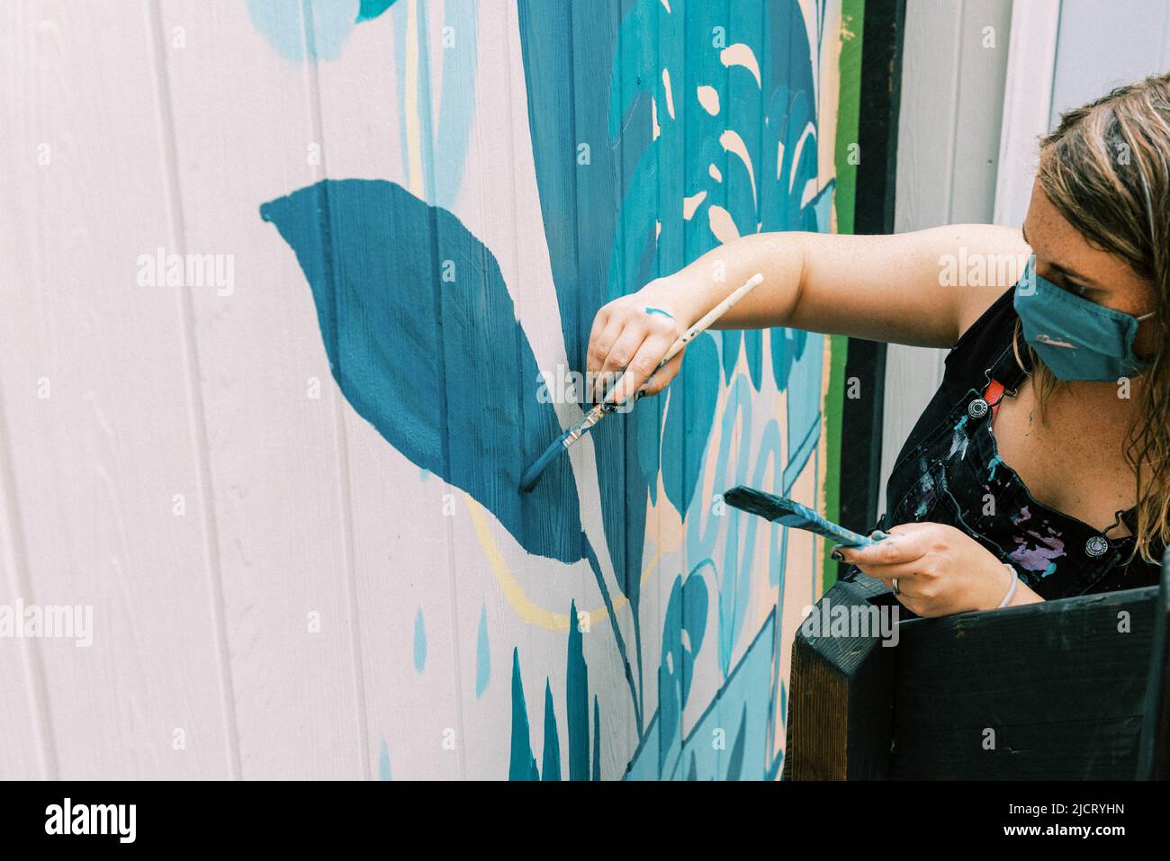 female artist painting a mural on wall of local business Stock Photo