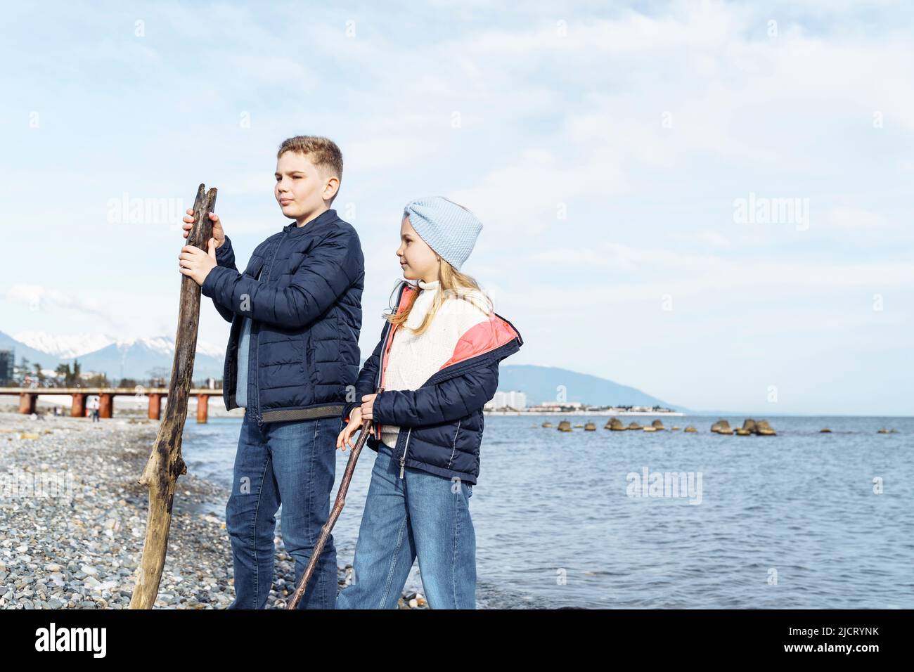 Brother and sister are walking on the seashore with sticks Stock Photo ...