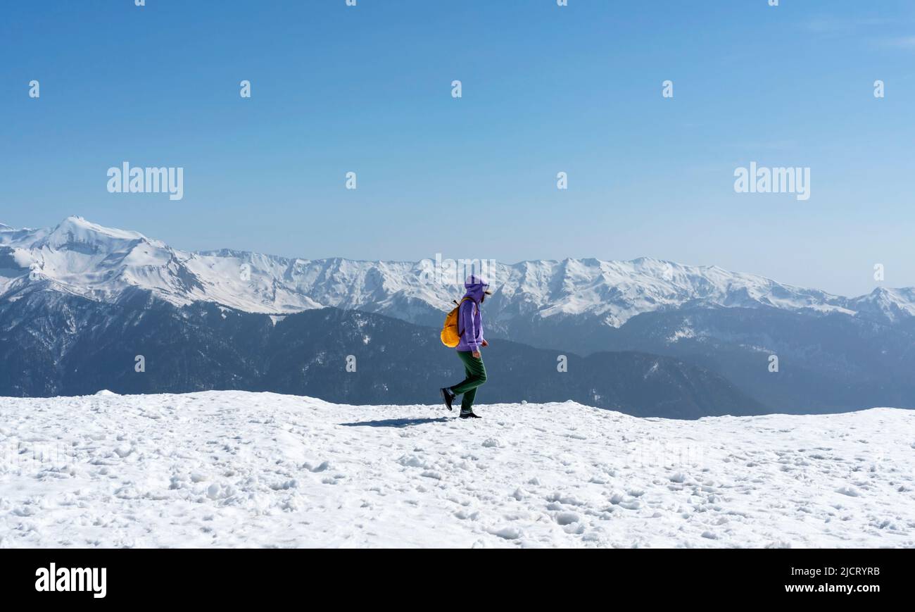 Young woman with yellow backpack walking in snowy mountains Stock Photo