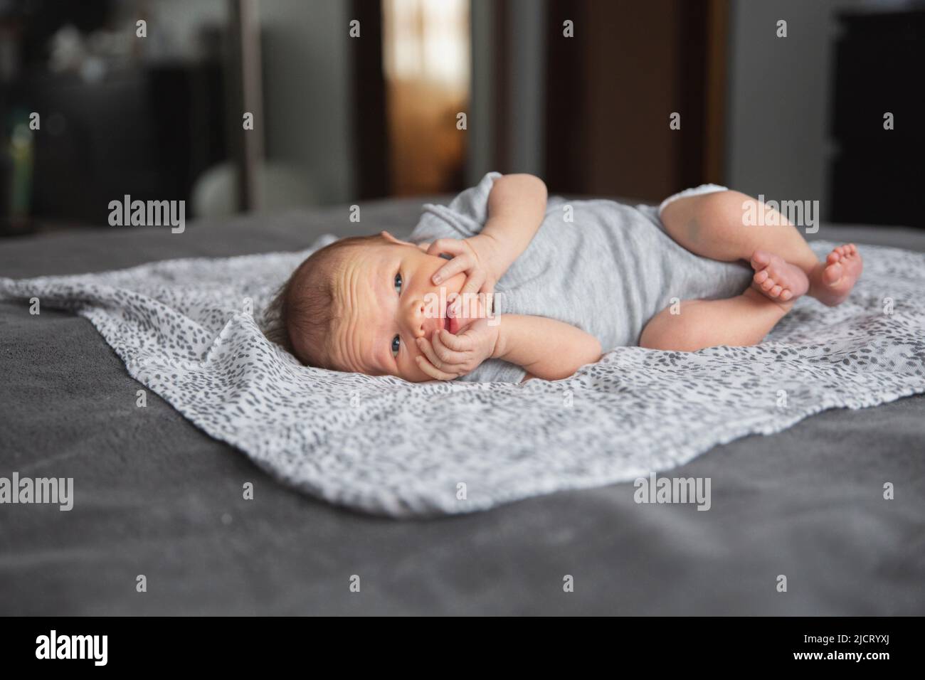 baby breezes on a big bed and touches his face with his hands Stock