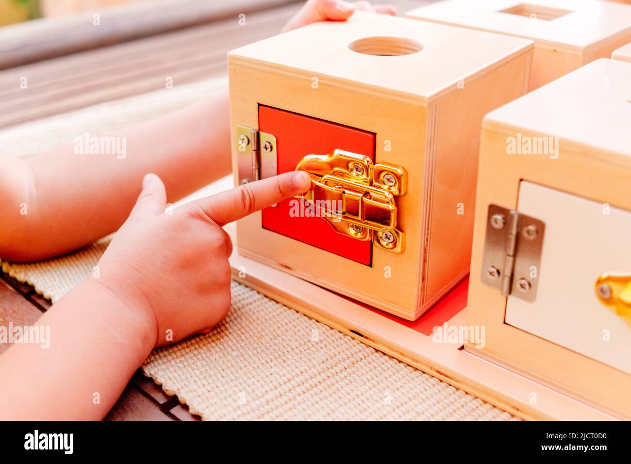 Little girl plays with a montessori educational material to open and close wooden boxes. Stock Photo