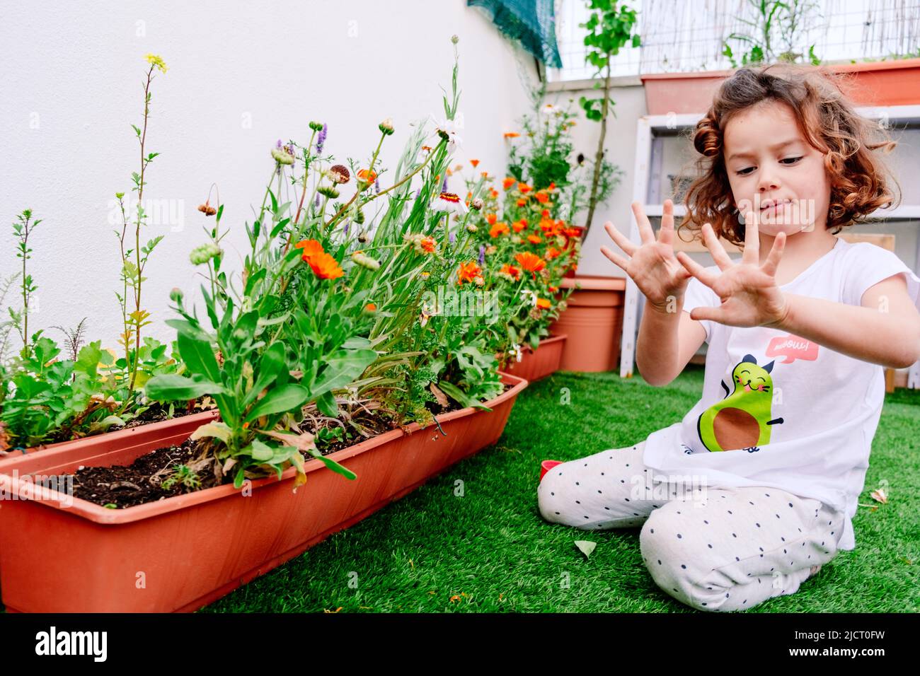 A girl takes care of her plants on the terrace of her apartment, watching them bloom in spring. Stock Photo