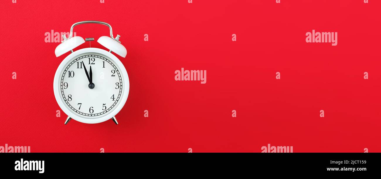 Alarm clock showing five minutes to twelve on red background. Copy