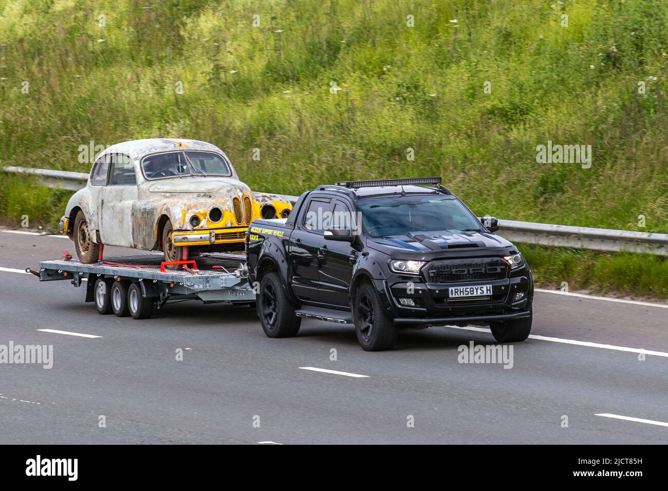 Ford Wildtrak towing old rusty 1950s Bristol 403 classic sedan, vintage vehicle on trailer; driving on the M6 Motorway, UK Stock Photo