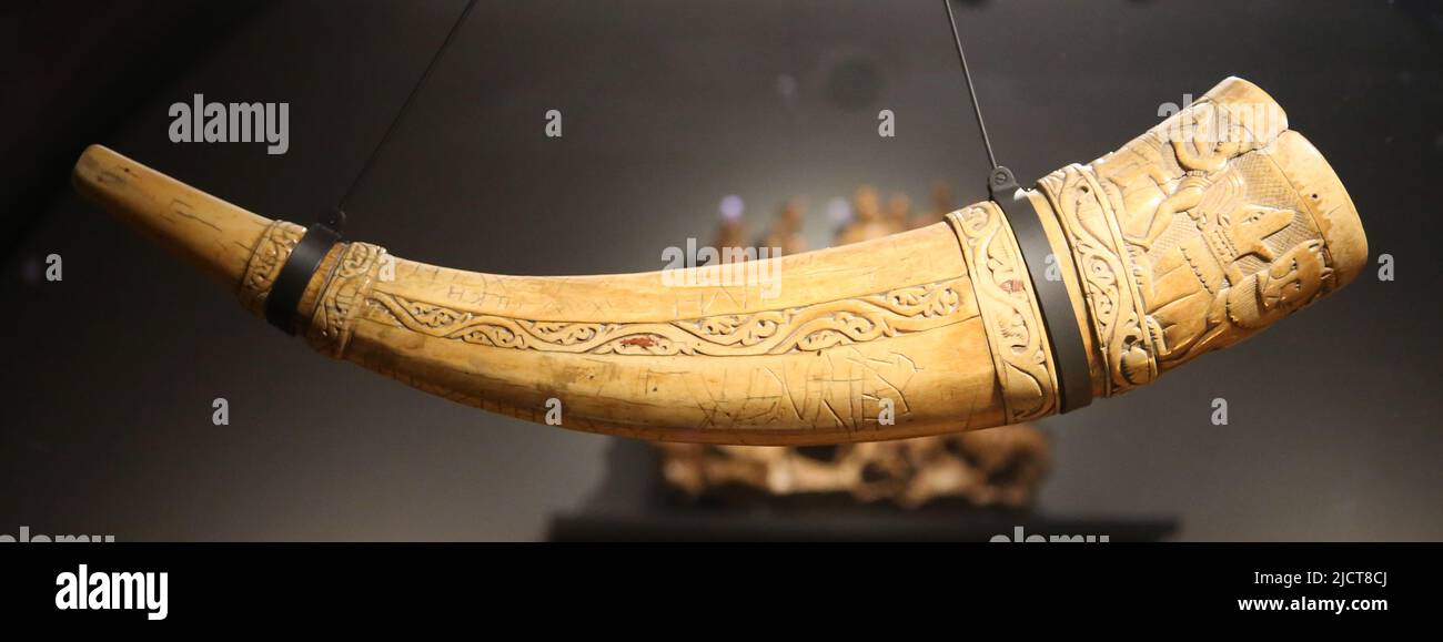 Hunting horn. Southern Italy, 11th century. Elephant tusk. Decorated with hunting scenes, around the wide end are two hunters attacking wild animals. Stock Photo