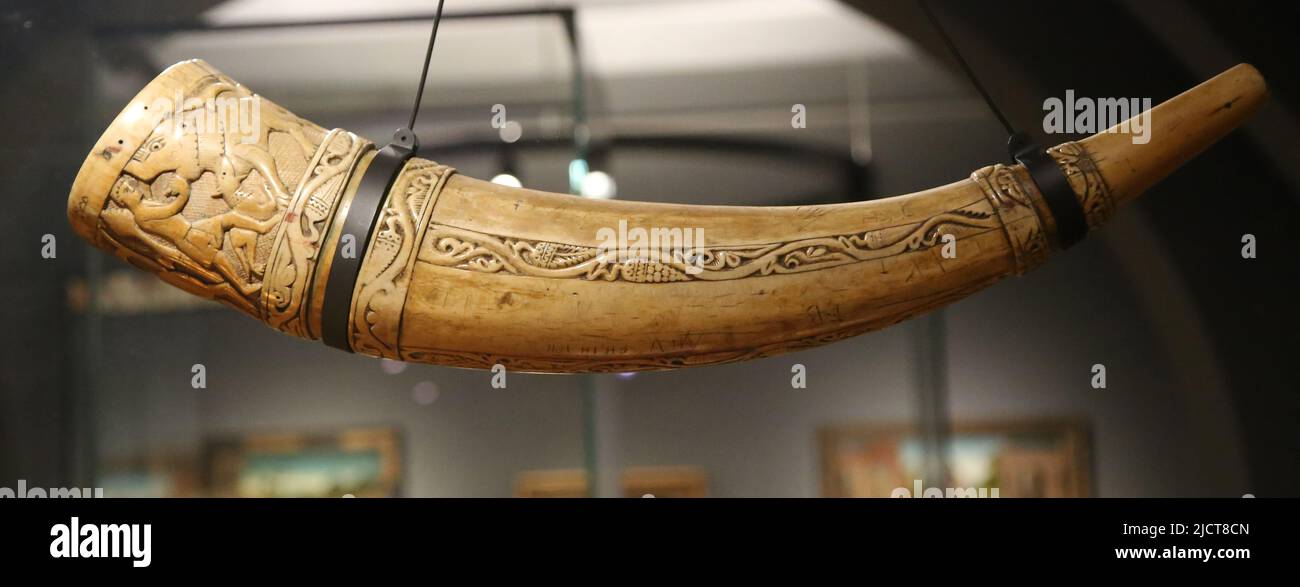 Hunting horn. Southern Italy, 11th century. Elephant tusk. Decorated with hunting scenes, around the wide end are two hunters attacking wild animals. Stock Photo