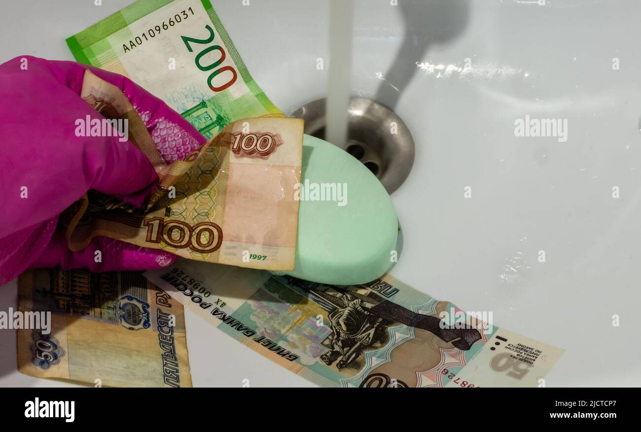 Hand in glove with soap on banknotes of russian rubles close-up under water jet in white ceramic wash basin. View from above Stock Photo