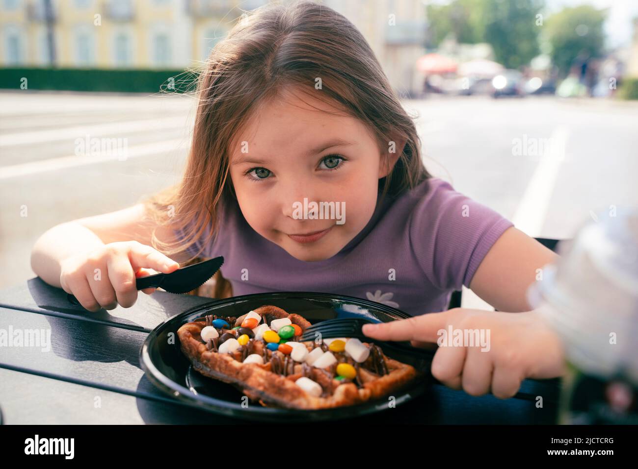 An 8 year old girl eats a Viennese waffle in a street cafe. High quality photo Stock Photo