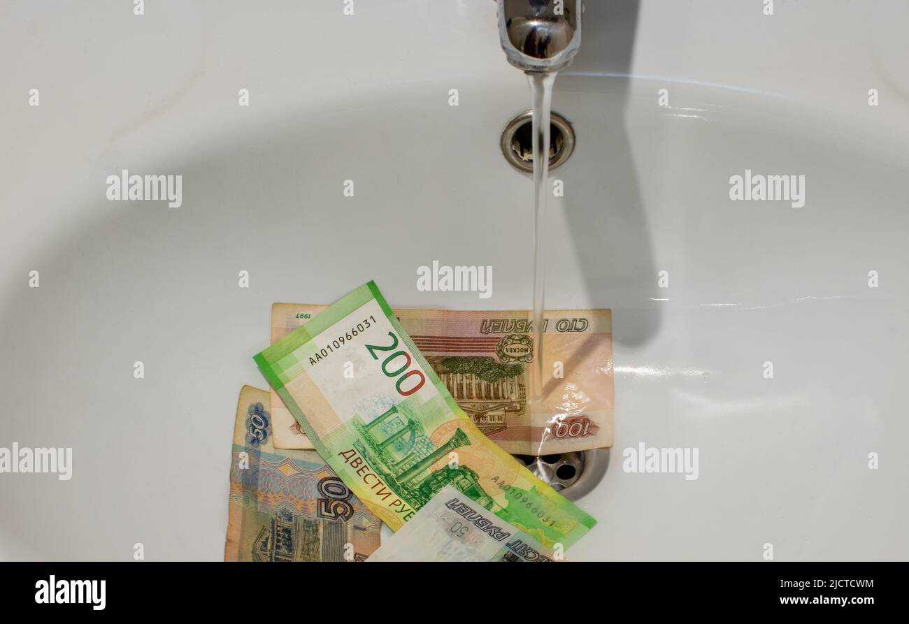 Banknotes of russian rubles close-up under water jet in a white ceramic washbasin. Top view Stock Photo