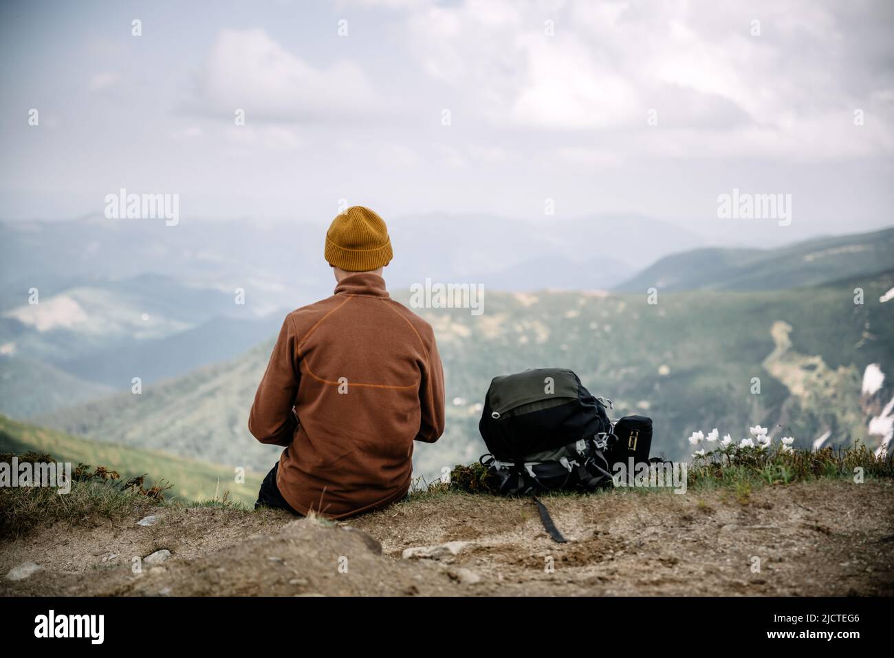 A tourist sits on the edge of a mountain peak. Foggy mountains on the background. Landscape photography Stock Photo