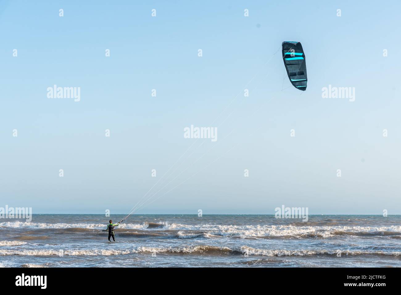 View of an unrecognizable man kitesurfing in the waves with a blue sky. Stock Photo